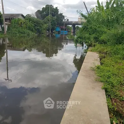 Scenic canal view with lush greenery and nearby residential structures.