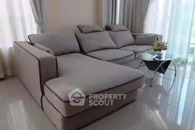 Elegant living room with plush grey sectional sofa, sleek glass coffee table, and airy sheer curtains, radiating modern luxury and comfort.
