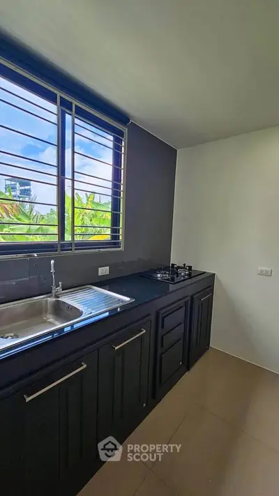 Modern kitchen with sleek black cabinetry and gas stove, featuring a large window with lush green views.