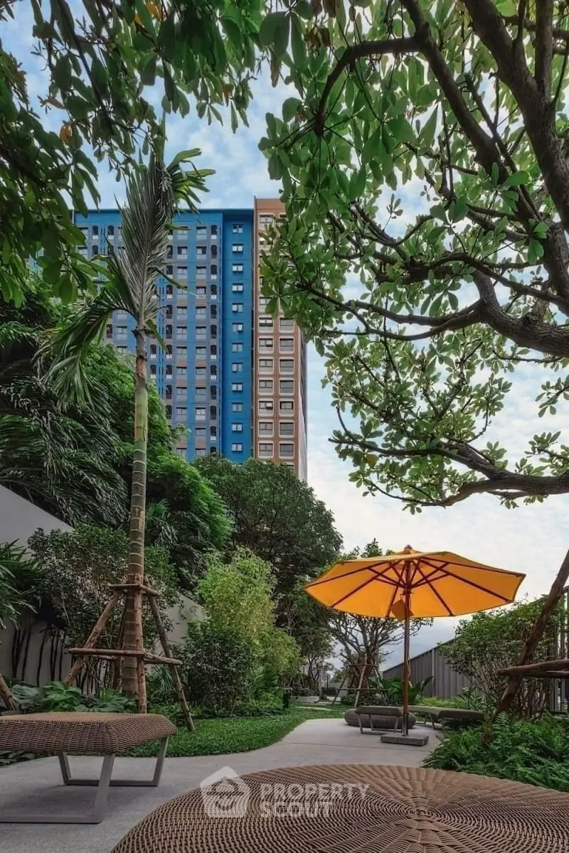 Lush garden with modern seating and vibrant umbrella in urban residential complex.
