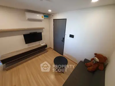 Cozy modern living room with wooden flooring, wall-mounted TV, and plush teddy bear on sofa.
