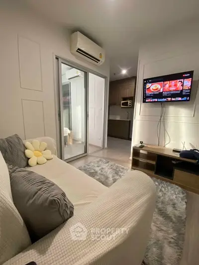Modern living room with cozy sofa, wall-mounted TV, and sleek kitchen in open layout apartment.
