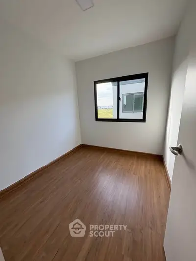 Spacious empty room with wooden flooring and large window offering natural light.