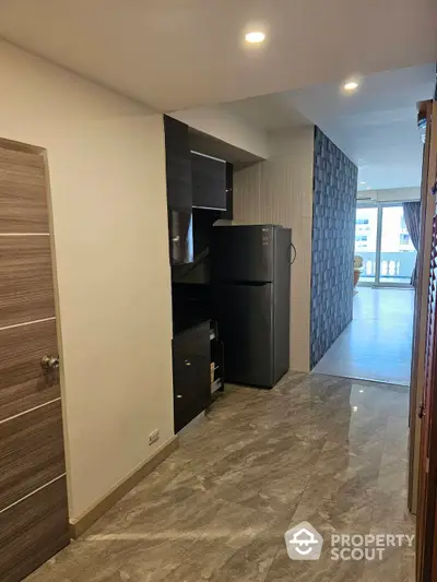 Modern kitchen with sleek black appliances, ample cabinetry, and polished marble flooring extending to a spacious balcony with natural light.