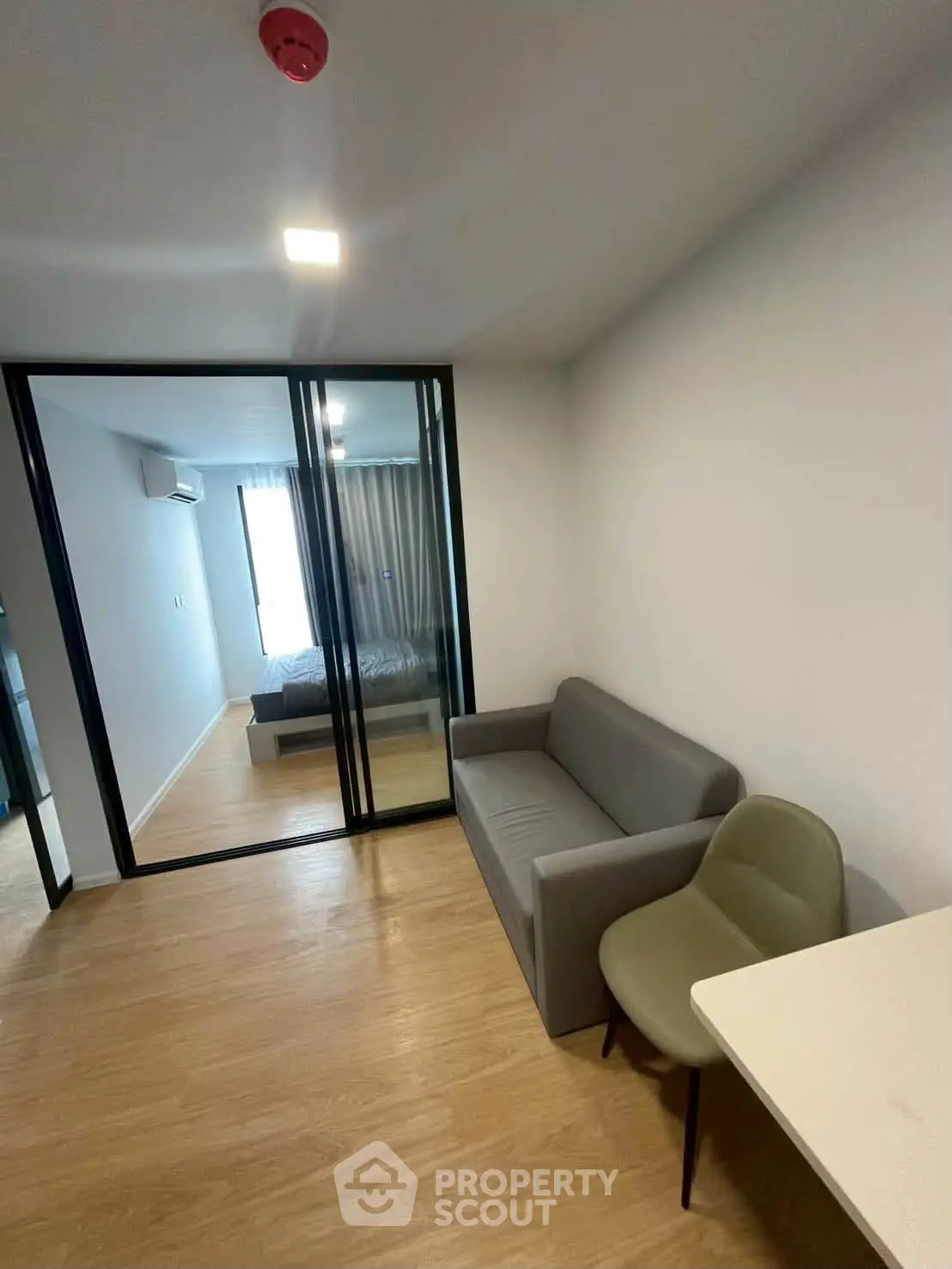 Modern apartment interior with glass partition, cozy living area, and bedroom view.