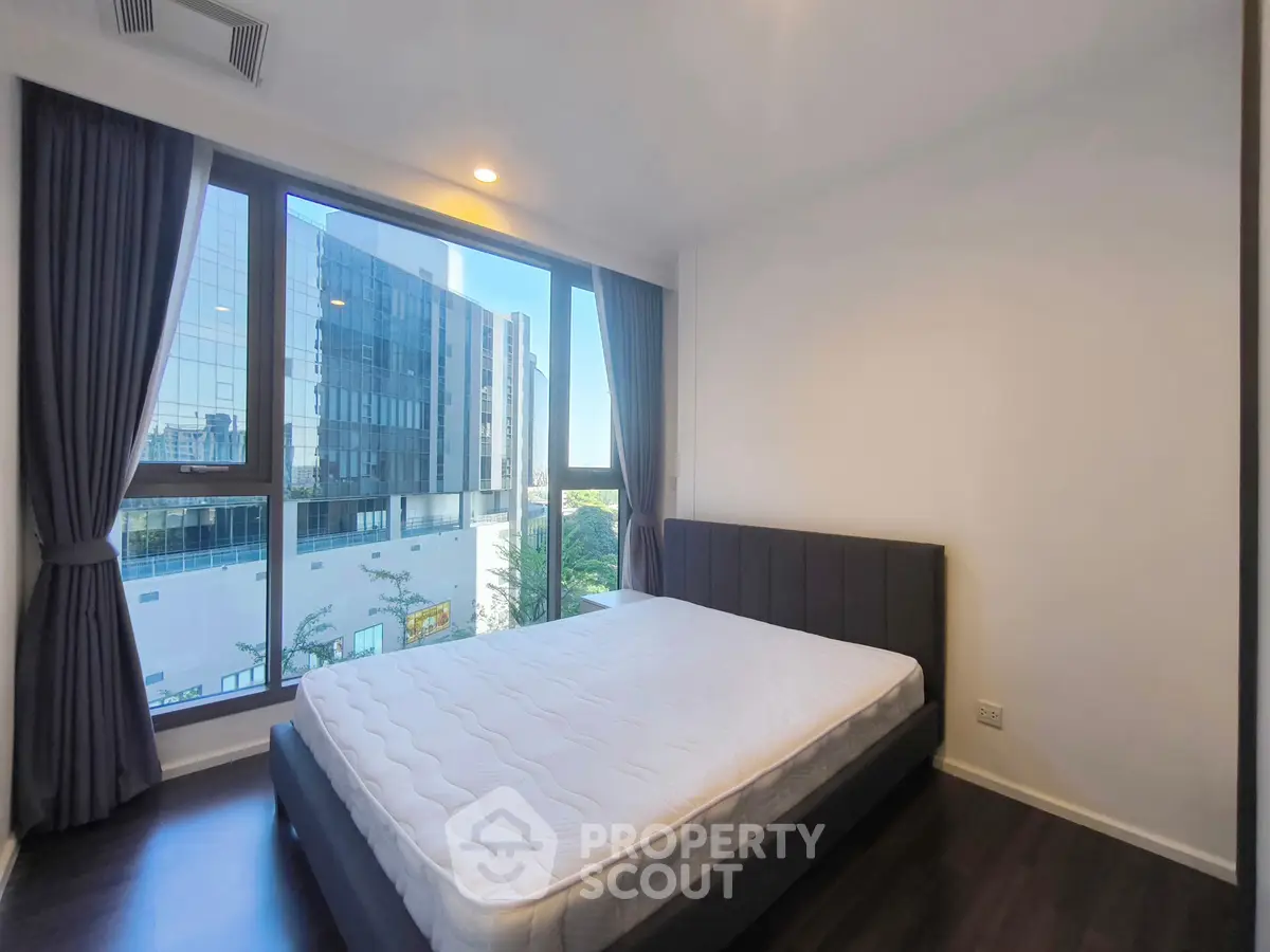 Spacious bedroom with large window offering stunning city view, modern design and ample natural light.