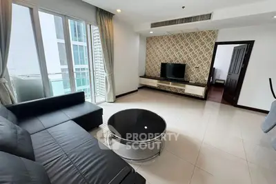 Spacious modern living room with sleek black sofa and large windows in a high-rise apartment.