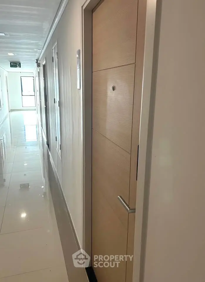 Modern apartment corridor with sleek wooden doors and glossy tiled flooring.