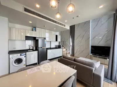 Modern open-plan living room with kitchen, featuring sleek design and natural light.