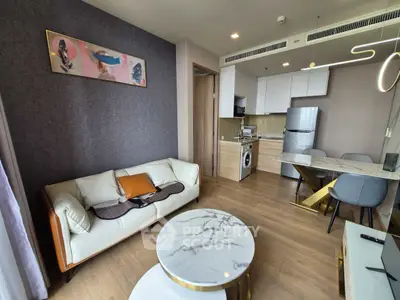 Modern living room with open kitchen, featuring stylish furniture and appliances.