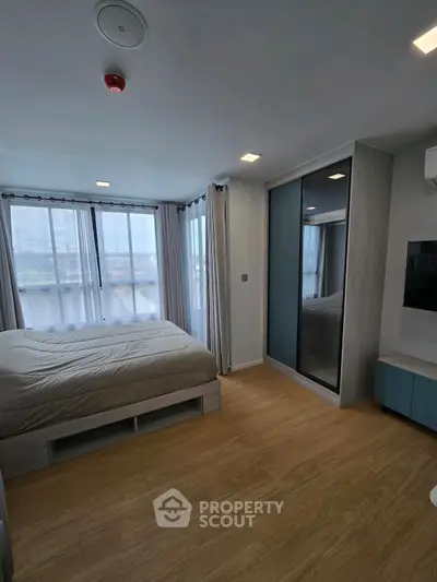 Modern bedroom with large windows and sleek furnishings in a high-rise apartment.