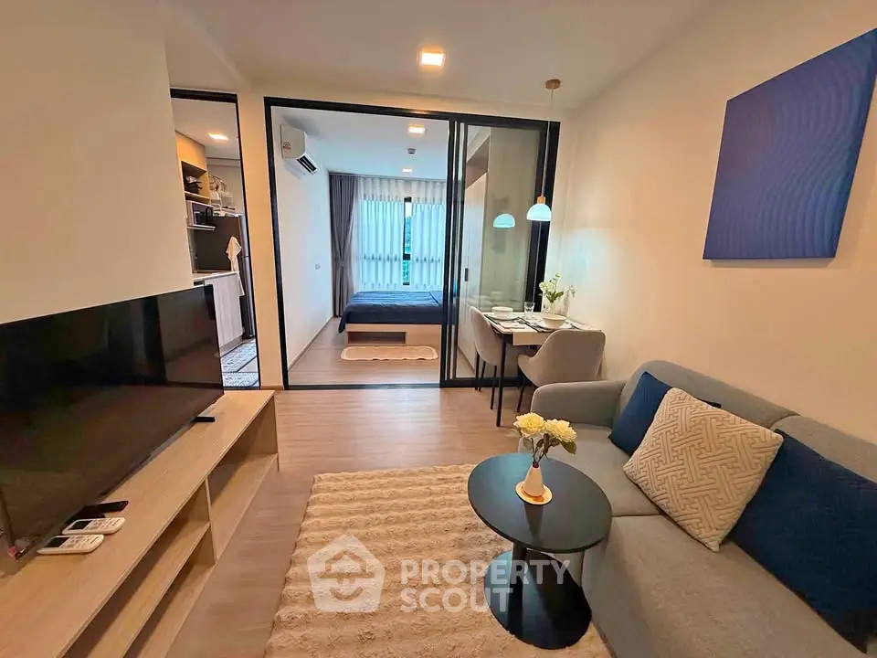 Modern living room with cozy sofa, TV, and view into stylish bedroom through glass doors.