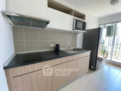 Modern kitchen with sleek cabinetry, built-in microwave, and large fridge in a bright apartment.