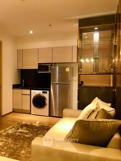 Modern living room with integrated kitchen featuring stainless steel appliances and cozy seating area.