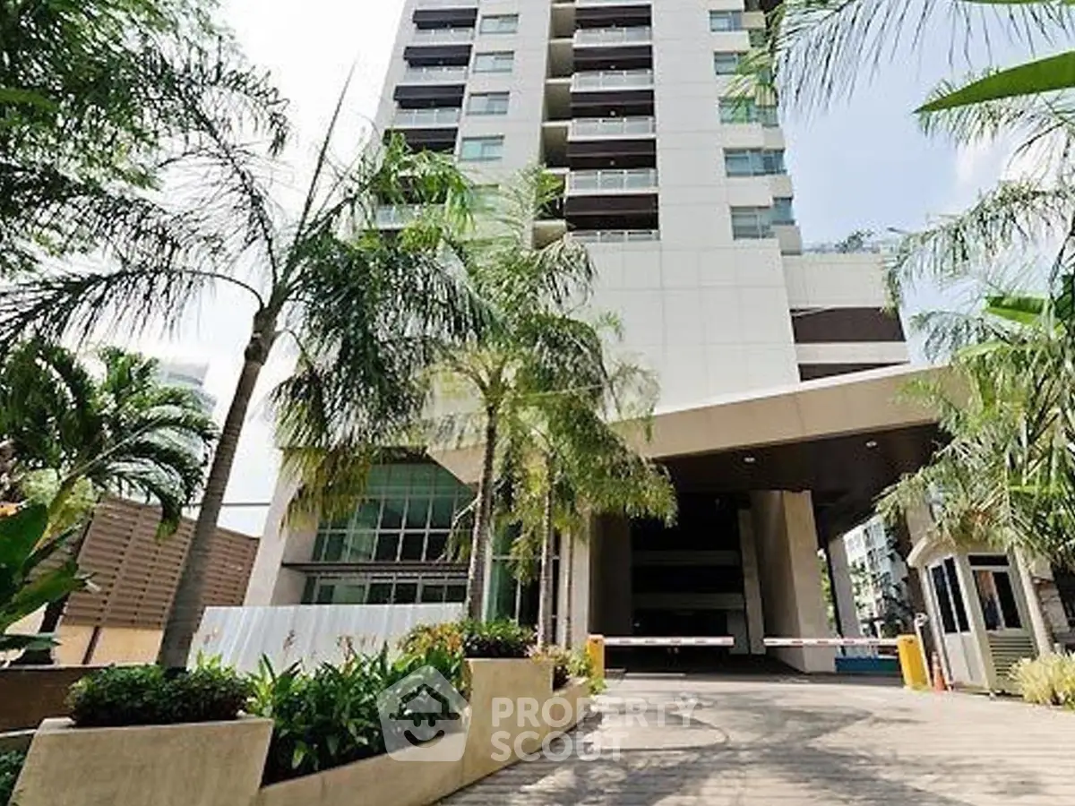Modern high-rise building entrance with lush landscaping and palm trees.
