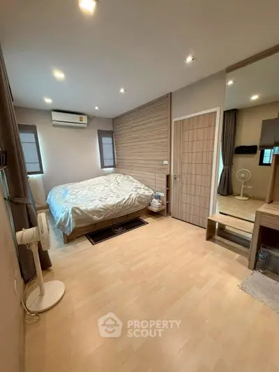 Spacious bedroom with modern decor and natural light, featuring wooden flooring and a cozy ambiance.