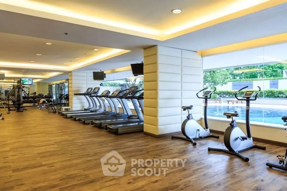 Luxurious gym with modern equipment and pool view in upscale residential complex.