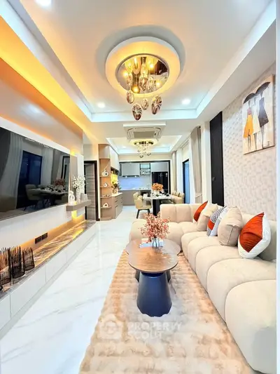 Luxurious modern living room with elegant lighting and plush furnishings, open layout leading to stylish kitchen.