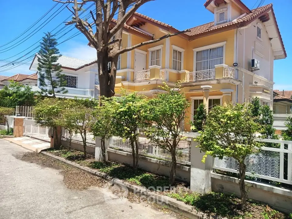 Charming two-story yellow house with lush garden and white fence in a serene neighborhood.