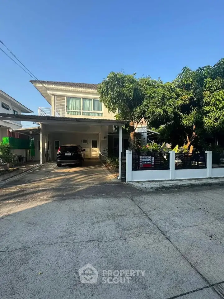 Charming two-story house with carport and lush greenery in a serene neighborhood.