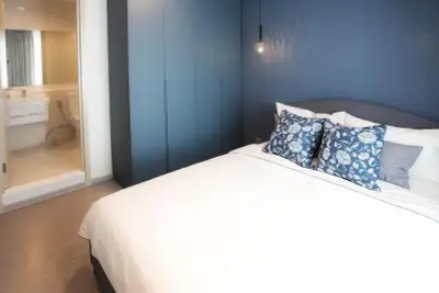 Modern bedroom with blue accent wall and ensuite bathroom in stylish apartment.