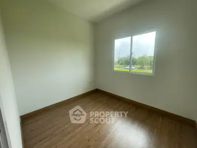 Spacious empty room with wooden flooring and large window offering natural light.