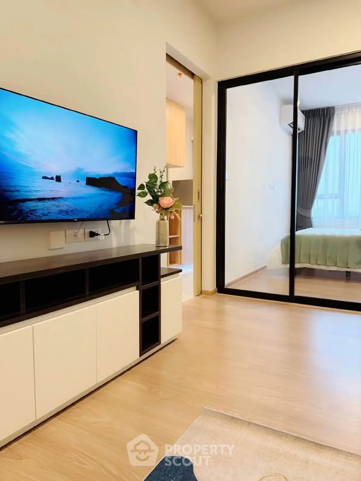 Modern living room with TV and sliding glass doors leading to a cozy bedroom.