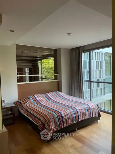 Modern bedroom with large windows and striped bedding in a stylish apartment.