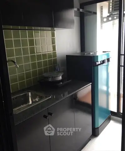 Compact kitchen with modern appliances and green tile backsplash in cozy apartment.