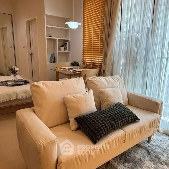 Cozy living room with beige sofa, stylish decor, and natural light through large windows.