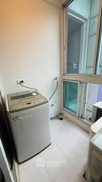 Compact laundry area with washing machine and large window in modern apartment.