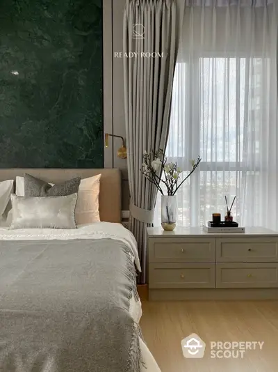 Elegant bedroom with a luxurious green marble wall accent, cozy bedding, and a classic dresser under a large window with sheer curtains, offering a serene ambiance.