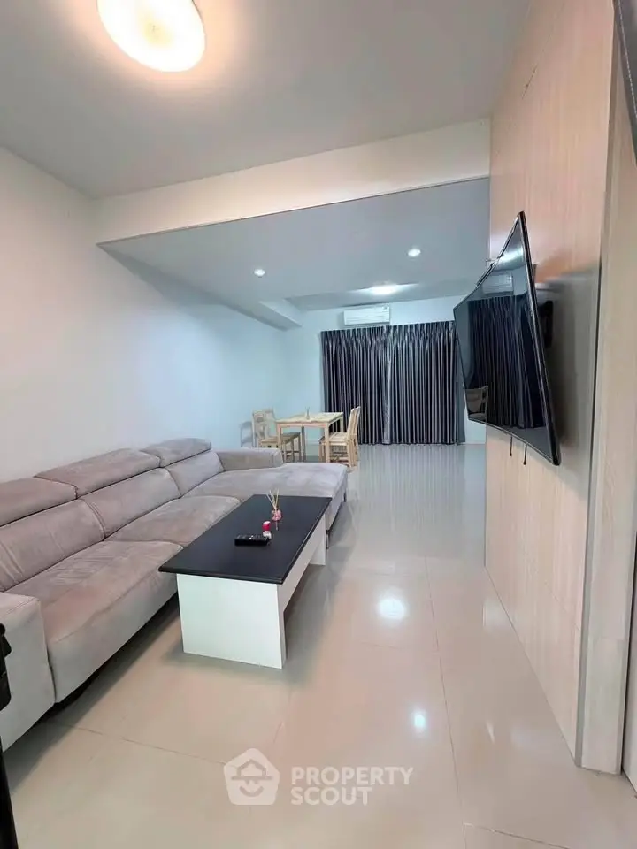 Spacious modern living room with sleek furniture and large TV, perfect for relaxation.