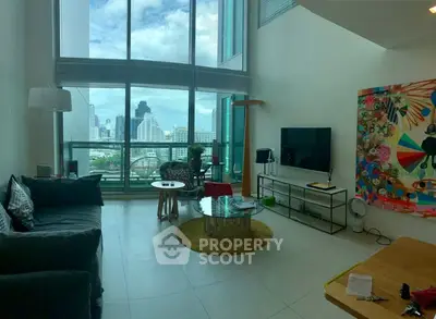Spacious modern living room with large windows and city view, featuring stylish decor and vibrant artwork.