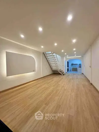 Spacious modern living room with wooden flooring and stylish staircase leading to upper level.