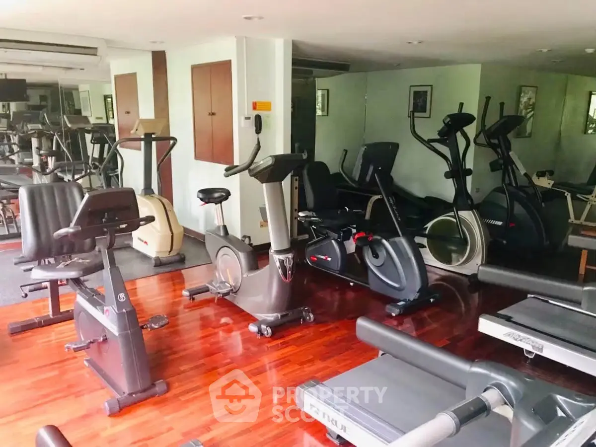 Spacious gym with modern exercise equipment and wooden flooring in a residential building.