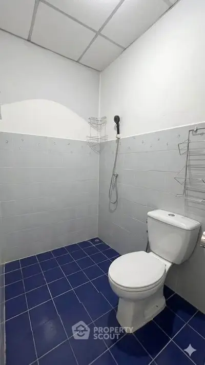 Minimalist bathroom with blue tiled floor and white walls, featuring a toilet and shower area.
