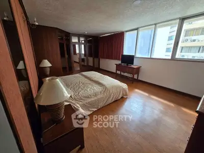 Spacious bedroom with large windows and wooden flooring in a modern apartment.