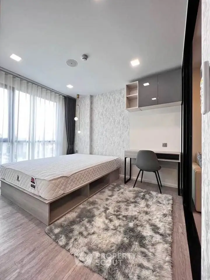 Modern bedroom with large window, stylish decor, and cozy rug in a contemporary apartment.