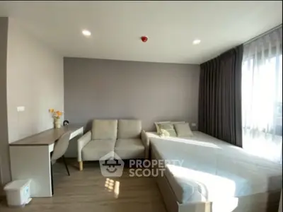 Modern bedroom with natural light, featuring a cozy sofa and work desk, ideal for urban living.