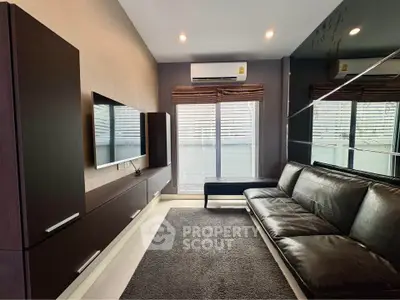 Modern living room with sleek black leather sofa and wall-mounted TV, featuring stylish dark wood cabinetry.