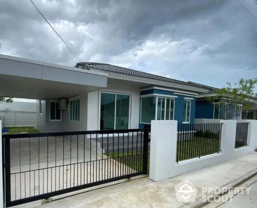 Modern single-story house with sleek design and spacious driveway under cloudy sky.