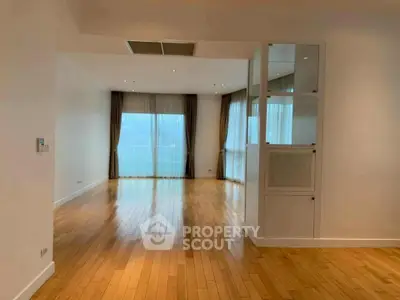 Spacious empty living room with wooden flooring and large windows.