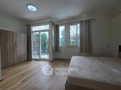 Spacious bedroom with large windows and balcony access, featuring wooden flooring and ample natural light.