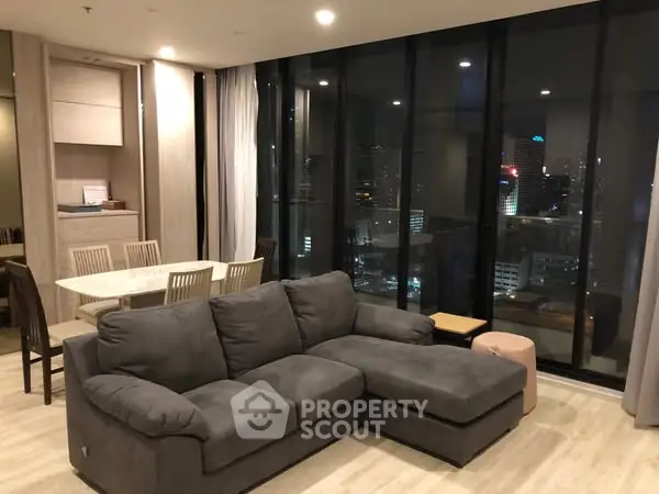 Modern living room with city view, featuring a spacious gray sectional sofa and elegant dining area.