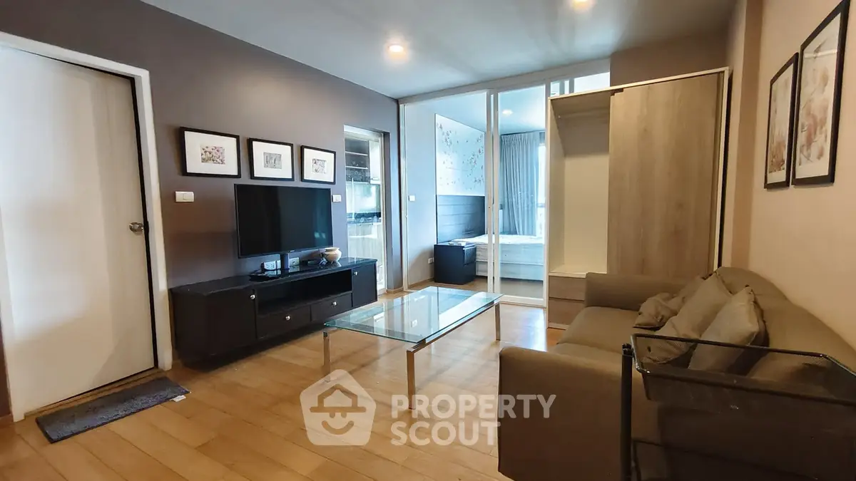 Modern living room with wooden flooring, glass coffee table, and cozy sofa, leading to a stylish bedroom.