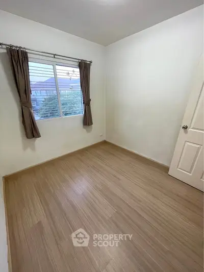 Spacious empty bedroom with wooden flooring and large window view.