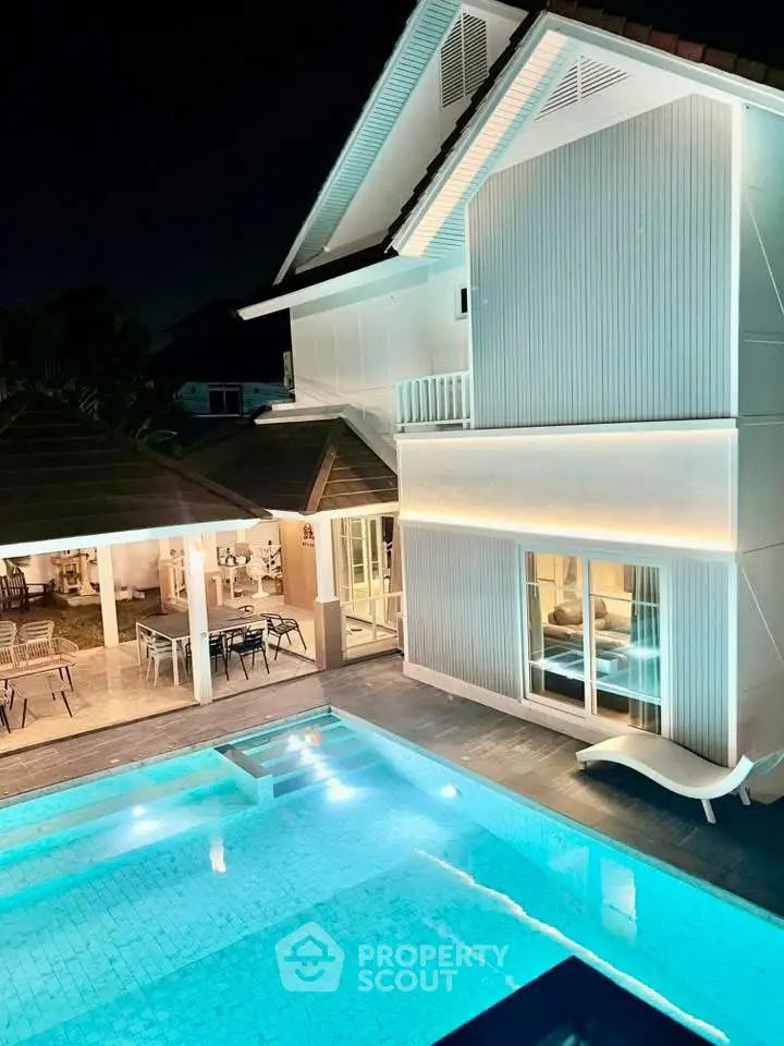 Luxurious modern home with illuminated pool and stylish outdoor seating area at night.