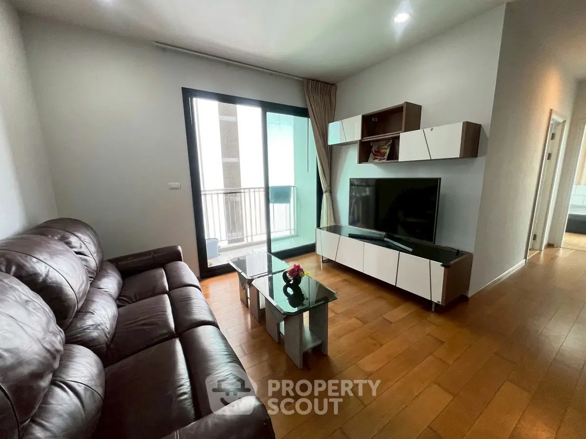 Modern living room with leather sofa, glass coffee table, and TV unit, featuring a balcony view.