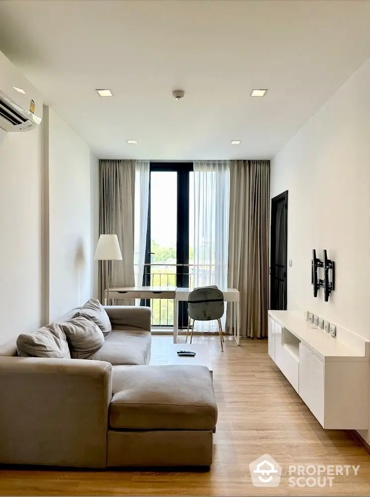 Spacious modern living room with natural light, sleek furniture, and a cozy ambiance, leading to a sunny balcony with a view.